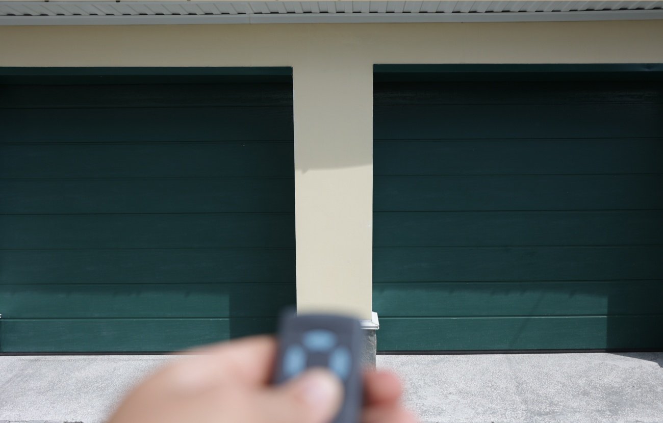 Person holding garage door opener with two green garage doors in back.