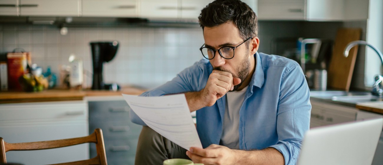 Man staring at paper electric bill with laptop open on kitchen table. Man staring at paper electric bill with laptop open on kitchen table.